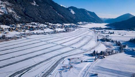 Verschneite Rennstrecke im Wintertal mit Bergen und einem Dorf im Hintergrund