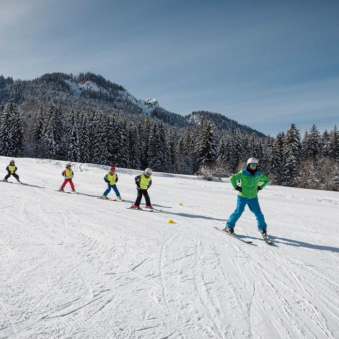 Skilehrer führt Kinder beim Skikurs auf verschneiter Piste in winterlicher Berglandschaft