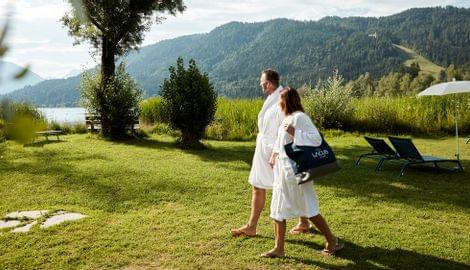 Paar in Bademänteln spaziert über Wiese am Seeufer mit Bergblick im Sommer