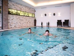 Zwei Personen schwimmen in einem modernen Innenpool mit dekorativer Steinwand