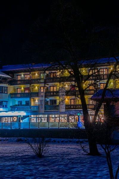 Beleuchtetes Hotel im Schnee mit weihnachtlicher Dekoration bei Nacht in den Alpen
