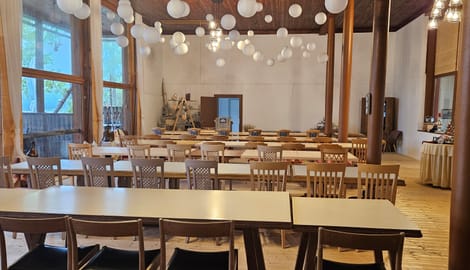 Rustic dining hall with wooden chairs, tables, and paper lanterns hanging from ceiling