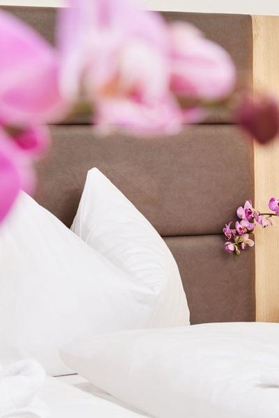 Modernes Hotelzimmer mit weißen Kissen, Orchideen und Handtuchdeko auf dem Bett