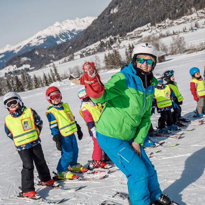 Skilehrer mit Handpuppe vor einer Gruppe Kinder in Skikurs auf verschneiter Piste in den Alpen