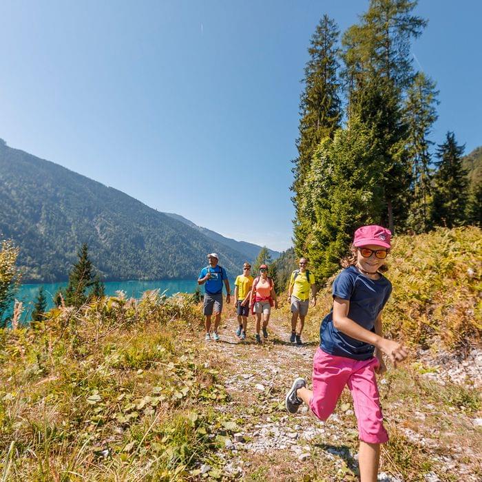 Familie wandert bei sonnigem Wetter auf einem Bergpfad am türkisblauen See