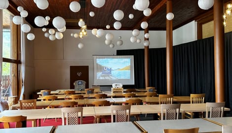 Konferenzraum mit Tischen, Stühlen und Leinwand, dekoriert mit weißen Papierlaternen