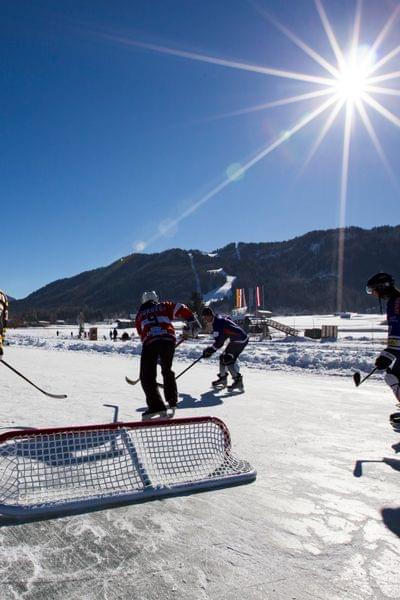 Eishockeyspiel im Freien bei Sonnenschein mit verschneiten Bergen im Hintergrund
