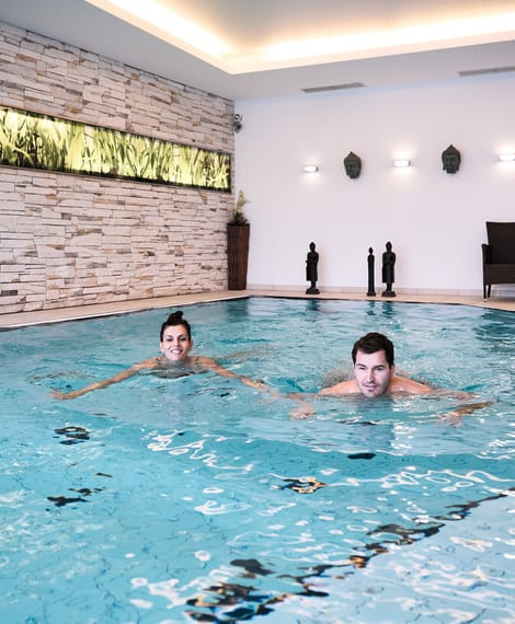 Zwei Personen schwimmen in einem modernen Innenpool mit dekorativer Steinwand