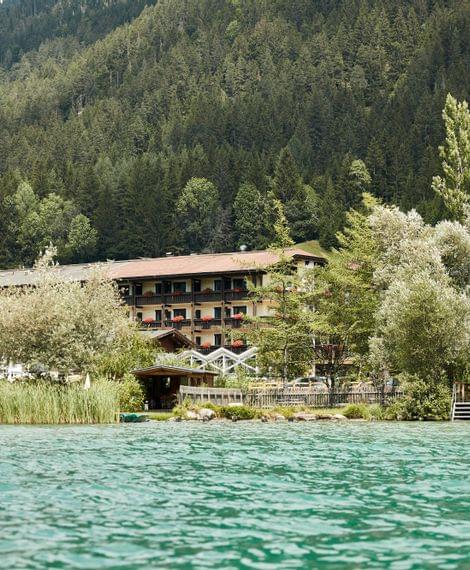 Hotel am Walchensee mit Bootshaus und Bergen im Hintergrund an einem Sommertag