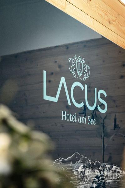 Hotellogo von Lacus Hotel am See an einer Holzverkleidungswand im Eingangsbereich