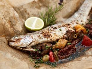 Gebackene Forelle mit mediterranem Gemüse, Kräutern und Limettenscheibe auf Backpapier serviert