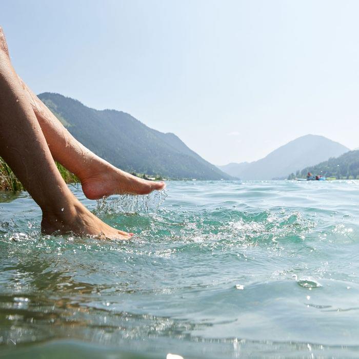 Füße tauchen in klares Wasser eines Bergsees mit Alpenpanorama im Sommer