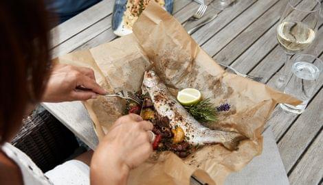 Gebackener ganzer Fisch mit Gemüse, Zitrone und Kräutern auf Pergamentpapier serviert