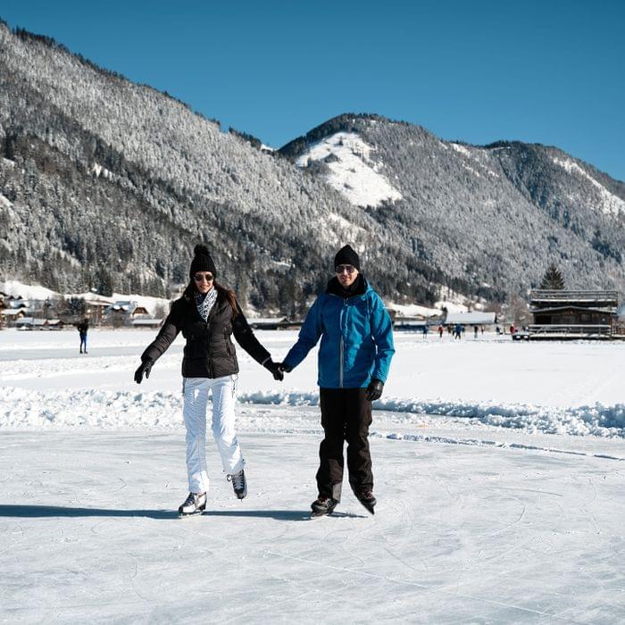 Paar beim Schlittschuhlaufen auf zugefrorenem See in verschneiter Berglandschaft