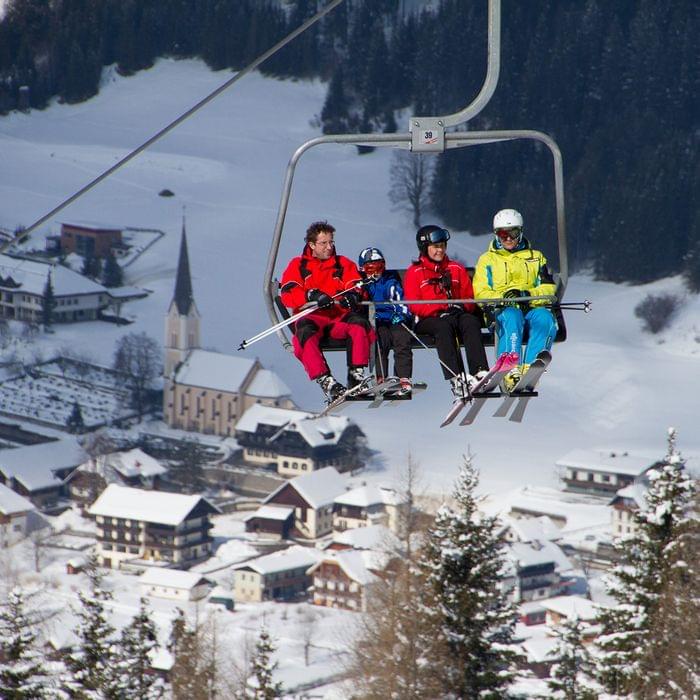 Skifahrer auf Sessellift über verschneitem Alpendorf mit Kirche und Häusern