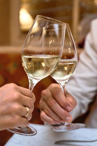 Zwei Menschen stoßen mit Weißweingläsern in einem eleganten Restaurant an