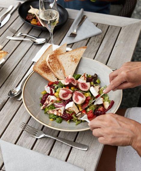 Frau isst frischen Salat mit Feigen, gegrilltem Toast und Sekt im Freien