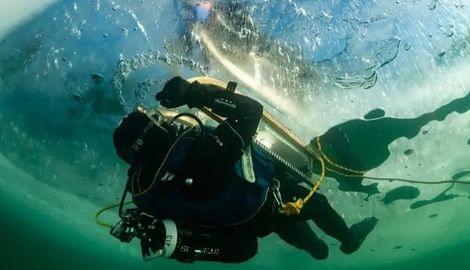 Taucher in Eistauchausrüstung unter einer gefrorenen Wasseroberfläche mit Sicherheitsleine