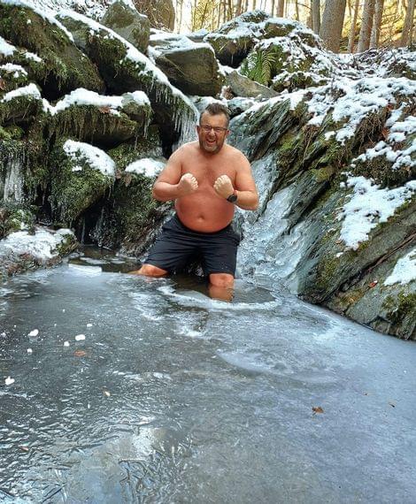 Mann kniet in gefrorenem Wasser vor schneebedecktem Wasserfall im Winterwald