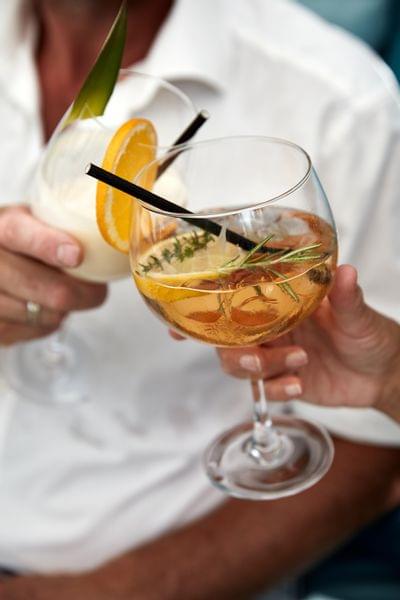 Two people toasting with cocktails garnished with orange slices and herbs