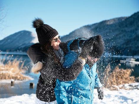 Frau und Mann haben Spaß bei einer Schneeballschlacht im Winter am verschneiten Seeufer