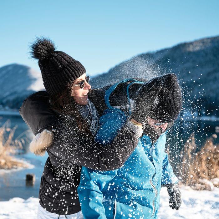 Frau und Mann haben Spaß bei einer Schneeballschlacht im Winter am verschneiten Seeufer