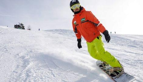 Snowboarder in orangefarbener Jacke und gelber Hose fährt schnell auf schneebedecktem Hang