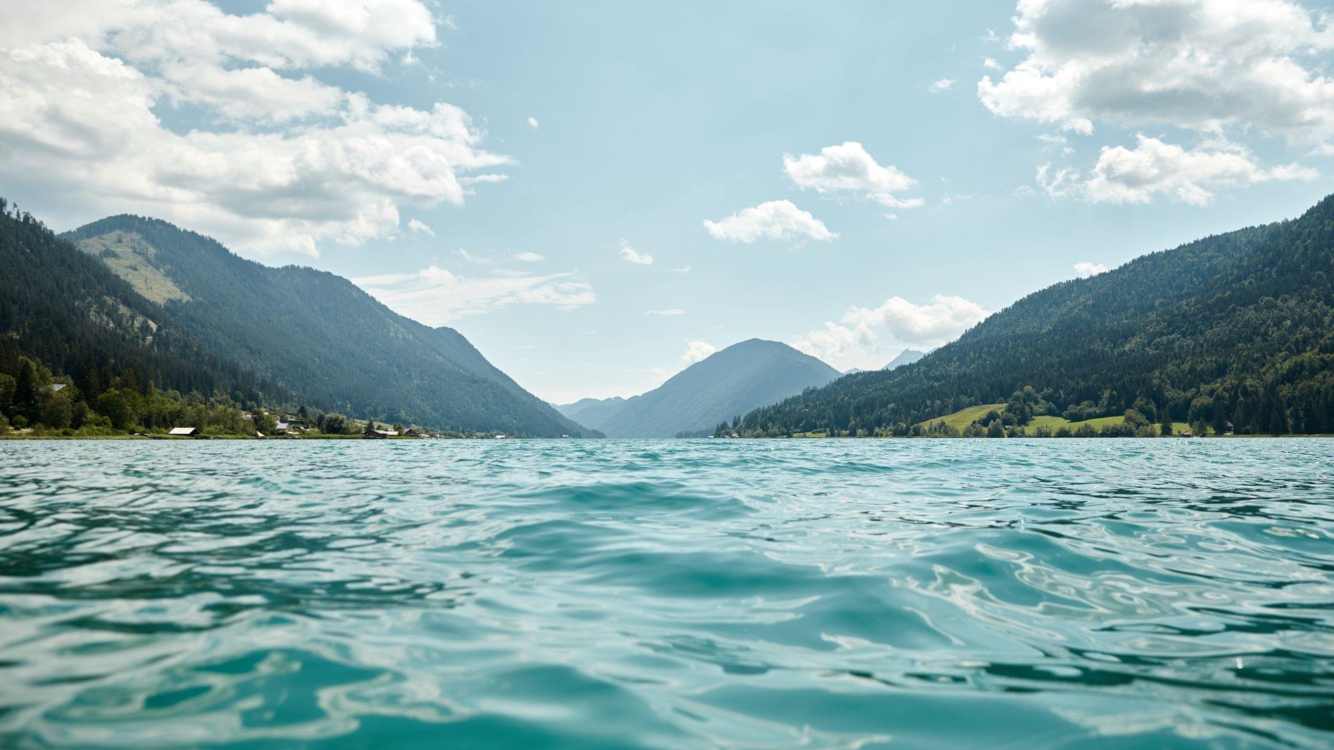Klares Bergseewasser mit umliegenden grünen Alpenhängen unter blauem Himmel