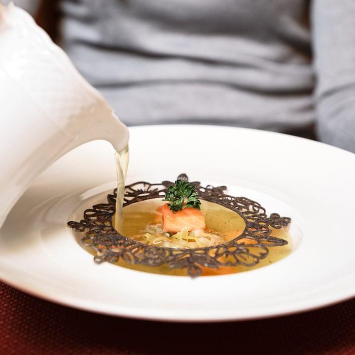 Feinsuppe mit Lachs, Gemüse und Garnitur, serviert mit Brühe in Gourmetrestaurant