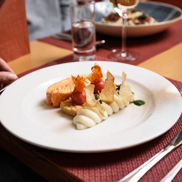 Gourmetgericht mit Lachsfilet, Püree und Gemüsekunst auf weißem Teller im Restaurant