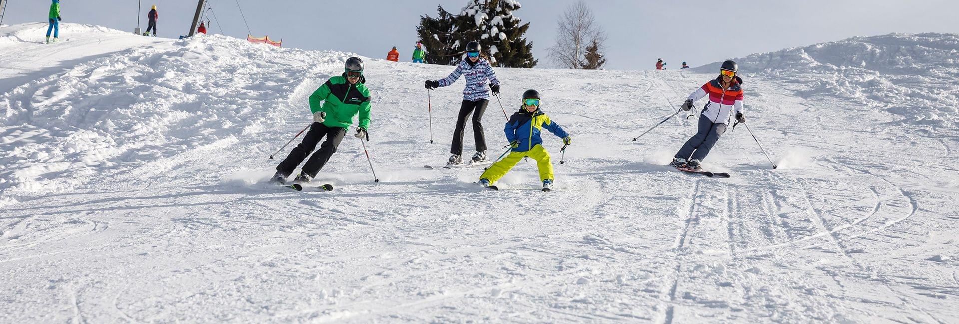 Vier Skifahrer fahren gemeinsam bei Sonnenschein eine verschneite Piste hinunter