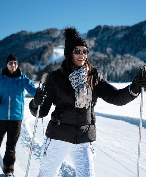 Zwei Langläufer auf verschneiter Loipe vor winterlicher Bergkulisse bei sonnigem Wetter