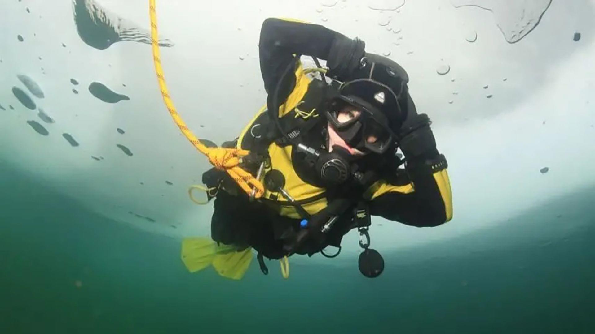 Taucher in Trockentauchanzug unter Eis mit Sicherheitsleine im kalten Wasser