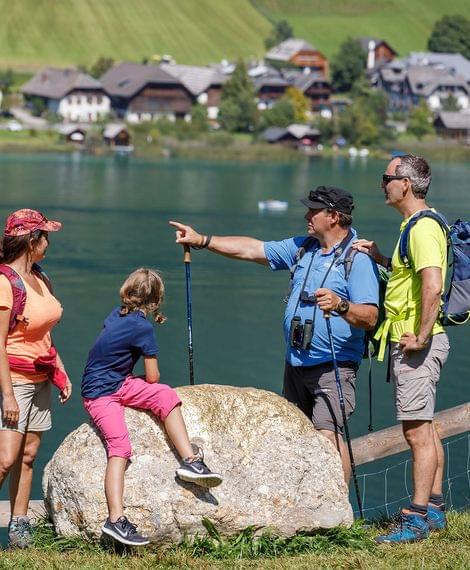 Gruppe von Wanderern mit Kind am Seeufer mit Alpenhäusern im Hintergrund