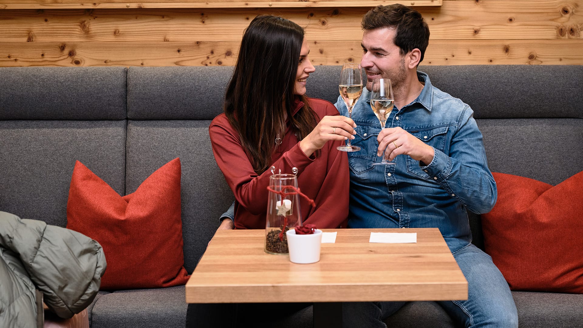 Paar stößt mit Sektgläsern in gemütlichem Restaurant mit Holzwand an