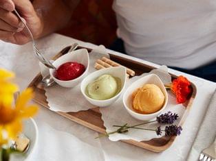 Drei Kugeln Eis in weißen Schalen mit Dekoblumen und Waffelröllchen auf Holztablett serviert